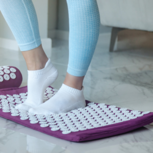 Acupressure mat with white nubs and purple cotton material pillow and mat view of a woman standing on the right