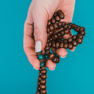 Mala beads hold by one hand against a blue background