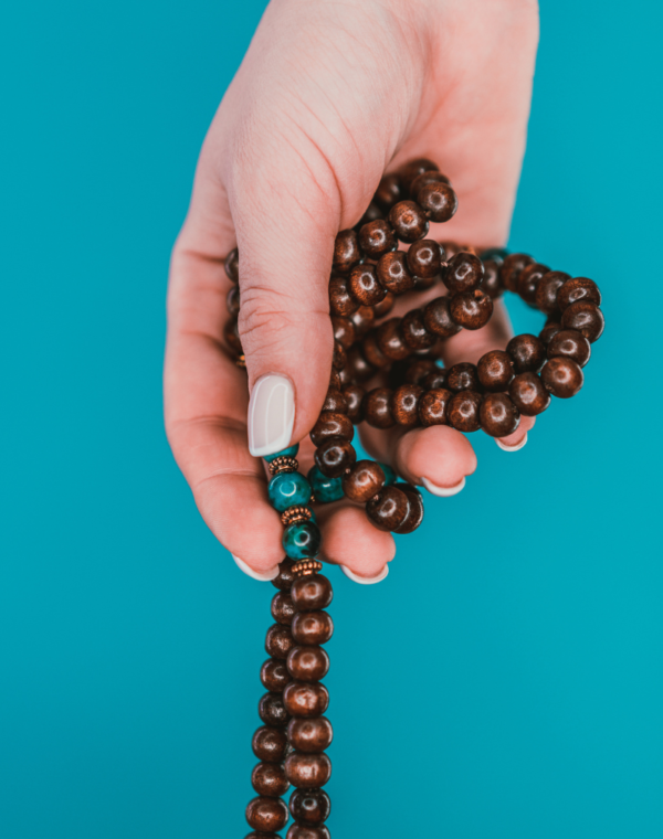 Mala beads hold by one hand against a blue background